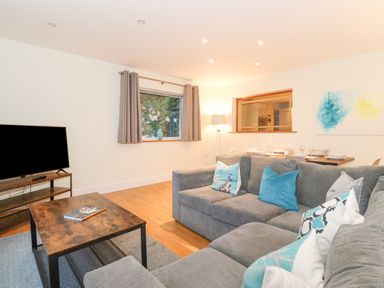 A living room with a gray sofa and blue pillows a wooden coffee table and a television on a stand at Tandarra in Keswick