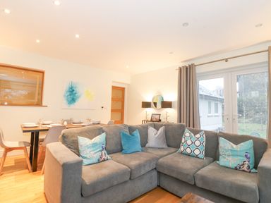 A living room with a grey sofa and colorful cushions near a dining table set with plates and glasses at Tandarra in Keswick