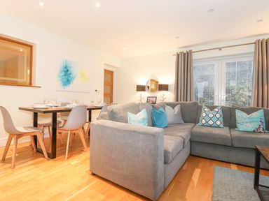 A living room with a grey sectional sofa and blue pillows next to a dining table with chairs and place settings at Tandarra in Keswick