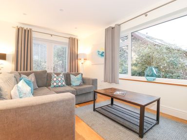 A living room with a gray sectional sofa and patterned cushions a wooden coffee table on a rug and large windows at Tandarra in Keswick
