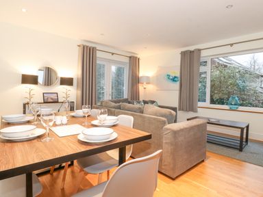A dining table set with plates and glasses in a room with sofas and large windows at Tandarra in Keswick