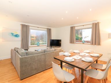 A living room with a grey sofa, a television, and a dining table set with plates and glasses at Tandarra in Keswick