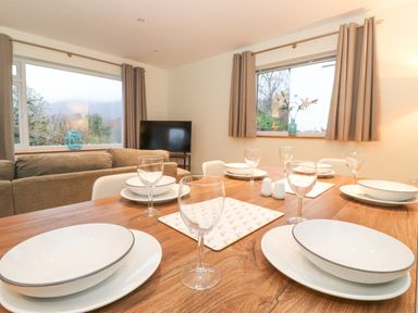 A dining table set with plates and glasses next to a living room with a sofa and television at Tandarra Keswick