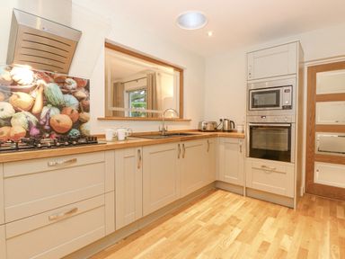 A kitchen with beige cabinets a gas stove a microwave an oven and a window at Tandarra Keswick
