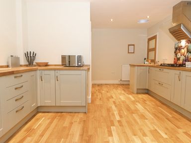 A kitchen with wooden floors white cabinets a microwave a knife block and a stove with a range hood at Tandarra in Keswick