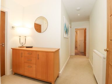 A hallway with a wooden cabinet and lamp under a round mirror at Tandarra in Keswick