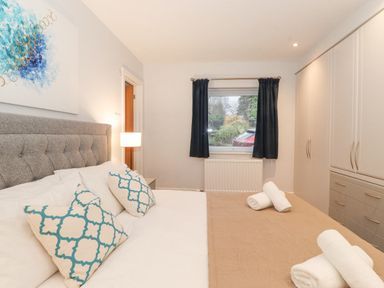A bedroom with a bed with patterned pillows a window with dark curtains and a wardrobe at Tandarra in Keswick