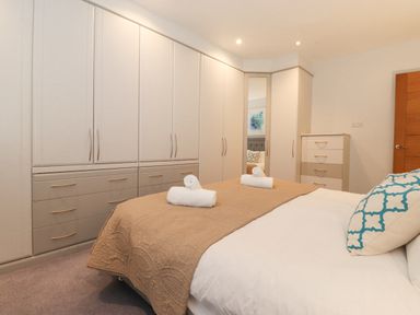 A bedroom with a bed with pillows and a beige quilt a large wardrobe a chest of drawers and a wooden door at Tandarra in Keswick