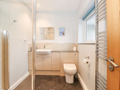 A bathroom with a toilet sink cabinets a window and a heated towel rail at Tandarra in Keswick