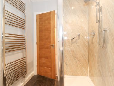 A bathroom with a wooden door a heated towel rail a shower area with marble walls and a glass screen at Tandarra in Keswick
