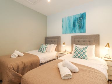 A bedroom with two beds with brown quilts and white pillows with blue patterned cushions two bedside tables with lamps and a blue painting on the wall at Tandarra in Keswick