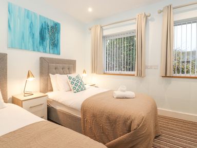 A bedroom with two single beds bedside tables lamps and two windows at Tandarra in Keswick