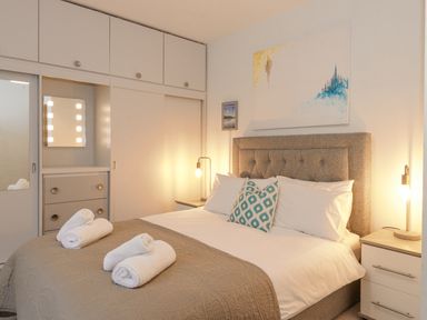 A bedroom with a bed with white sheets and a brown quilt two bedside tables with lamps and a built-in wardrobe with drawers and sliding doors at Tandarra in Keswick