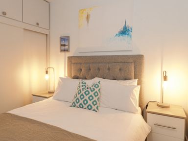 A bedroom with a bed with headboard two bedside tables with lamps and wall art at Tandarra in Keswick