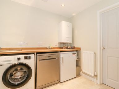 A utility room with a washing machine dishwasher small fridge radiator and boiler at Tandarra Keswick