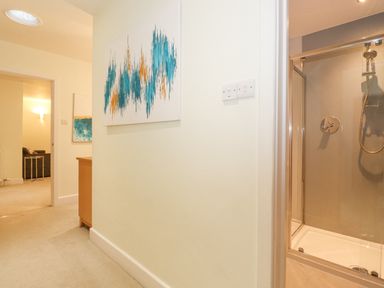 A hallway with a painting on the wall a wooden cabinet a view into a living room and a shower enclosure at Tandarra in Keswick