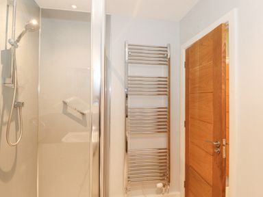 A bathroom with a shower cabin and a chrome heated towel rail next to a wooden door at Tandarra in Keswick