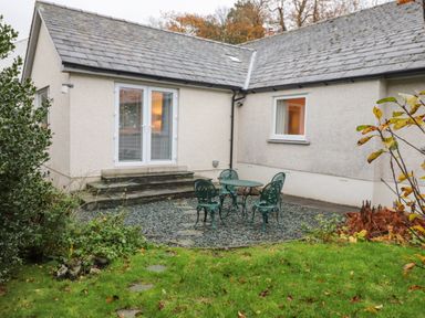 An outdoor patio with green metal table and chairs on gravel next to a house with white walls and grey roof at Tandarra in Keswick