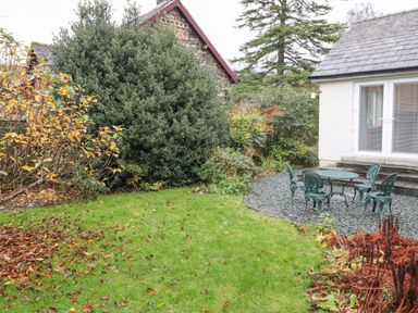 A garden with green grass a metal table with four chairs on gravel outside a house at Tandarra in Keswick