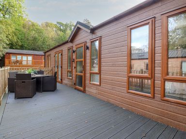 A wooden deck outside a brown cabin with outdoor dining furniture at Snuggledown Troutbeck 5 White Cross Bay near Windermere