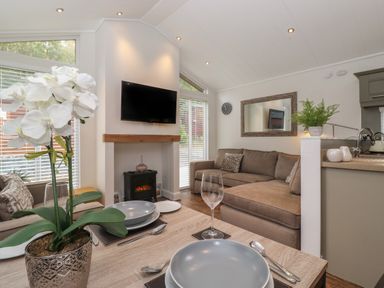 A dining table set with plates and glasses near a living room with a brown sofa a wall-mounted TV and a small fireplace at Snuggledown Troutbeck 5 White Cross Bay near Windermere