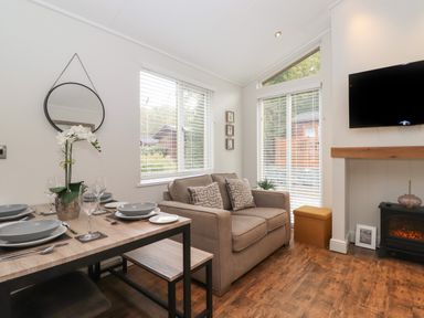 A dining table set with plates and glasses next to a sofa and a wall-mounted TV at Snuggledown in Troutbeck 5 White Cross Bay near Windermere
