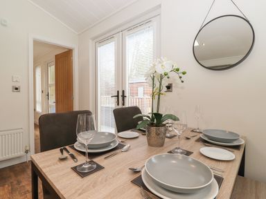 A dining table set with plates glasses and cutlery with a plant on it in a room with a round mirror at Snuggledown Troutbeck 5 White Cross Bay near Windermere