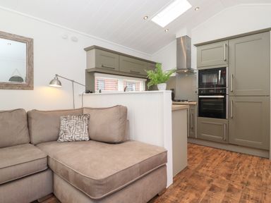 A living room with a beige sectional sofa and a lamp next to a kitchen with green cabinets and built-in appliances at Snuggledown Troutbeck 5 White Cross Bay near Windermere