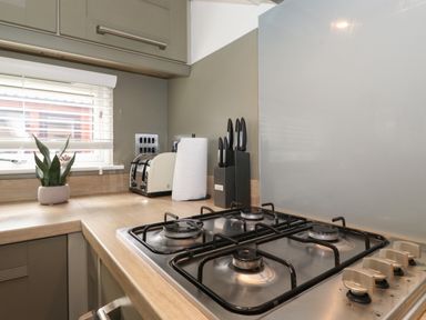 A kitchen counter with a gas stove a knife block a roll of paper towels a toaster and a potted plant near a window at Snuggledown in Troutbeck 5 White Cross Bay near Windermere