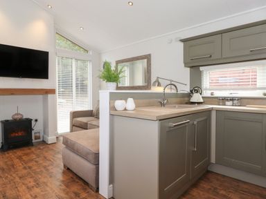 A kitchen with cabinets and a sink next to a living area with a sofa a television and a small fireplace at Snuggledown in Troutbeck 5 White Cross Bay near Windermere