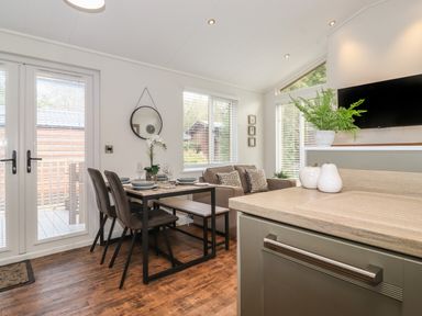 A dining table with chairs and bench next to a sofa in a room with windows and a TV at Snuggledown in Troutbeck 5 White Cross Bay near Windermere