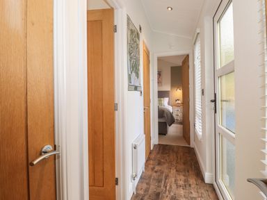 A hallway with wooden doors leading to a bedroom with a bed and bedside table at Snuggledown Troutbeck 5 White Cross Bay near Windermere
