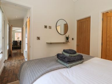 A bedroom with a bed covered with a quilt and folded towels on top three wooden doors and a small round mirror on the wall at Snuggledown in Troutbeck 5 White Cross Bay near Windermere
