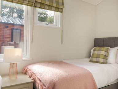 A bedroom with a single bed a pink blanket and a green checkered cushion at Snuggledown Troutbeck 5 White Cross Bay near Windermere