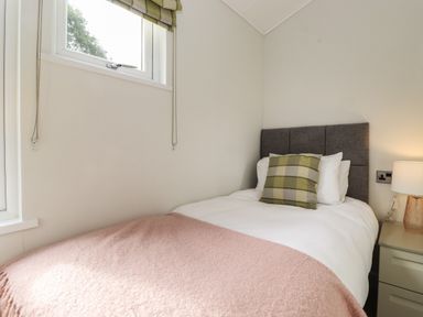 A bedroom with a single bed a green checked pillow a pink blanket a bedside table and lamp at Snuggledown Troutbeck 5 White Cross Bay near Windermere