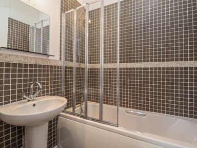 A bathroom with a white pedestal sink and a bathtub with a glass shower screen and tiled walls at Snuggledown Troutbeck 5 White Cross Bay near Windermere