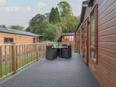 An outdoor deck with a table and four chairs beside wooden lodges and trees at Snuggledown in Troutbeck 5 White Cross Bay near Windermere