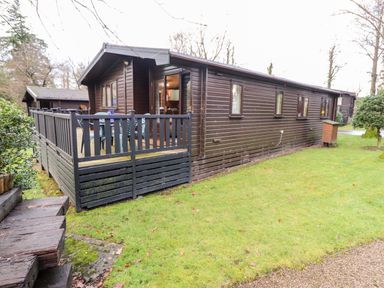 A wooden cabin with a fenced deck and plastic chairs on a grass lawn at Latrigg Lodge Number 9 Burnside Park near Keswick