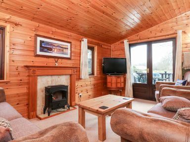 A living room with wood panel walls a fireplace a wooden coffee table a television and glass doors at Latrigg Lodge Number 9 Burnside Park near Keswick