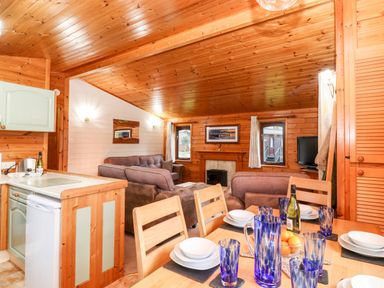A dining table set with blue glasses and white dishes in a wooden living area with sofas and a fireplace at Latrigg Lodge Number 9 Burnside Park near Keswick