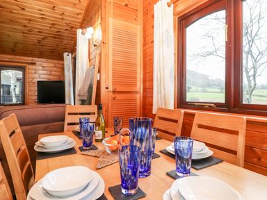 A dining table set with blue glasses and white plates in a wooden interior with windows showing an outdoor view at Latrigg Lodge Number 9 Burnside Park near Keswick
