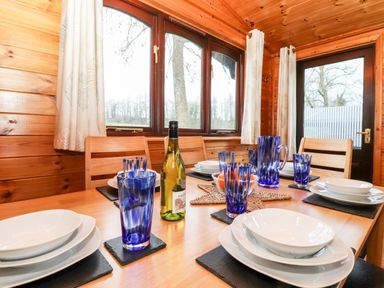 A dining table set with blue glasses white plates and a bottle of wine in a wooden room at Latrigg Lodge Number 9 Burnside Park near Keswick