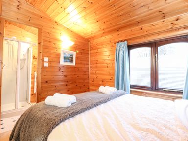 A bedroom with wooden walls a bed with towels and a window with blue curtains at Latrigg Lodge Number 9 Burnside Park near Keswick