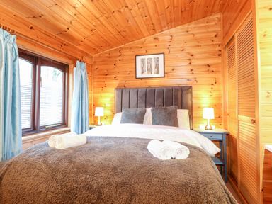 A bedroom with a double bed two bedside tables lamps a window with curtains and wooden walls at Latrigg Lodge Number 9 Burnside Park near Keswick