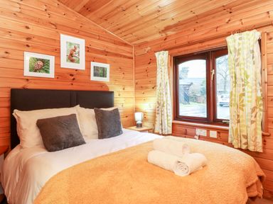 A bedroom with a double bed pillows rolled towels framed pictures and a window with curtains at Latrigg Lodge Number 9 Burnside Park near Keswick