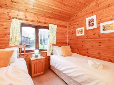 A bedroom with two single beds a wooden nightstand and framed pictures on the wood-paneled walls at Latrigg Lodge Number 9 Burnside Park near Keswick