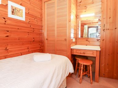A bedroom with a single bed a white blanket a towel a wooden wardrobe a wooden dressing table with a mirror and two wooden stools at Latrigg Lodge Number 9 Burnside Park near Keswick