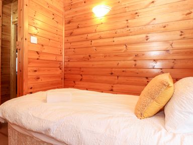 A bedroom with wooden paneled walls a bed with white bedding and a yellow pillow at Latrigg Lodge Number 9 Burnside Park near Keswick