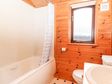 A bathroom with a bathtub a shower curtain a toilet a sink and a window with wooden walls at Latrigg Lodge Number 9 Burnside Park near Keswick