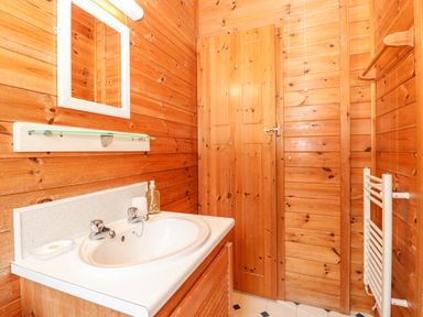 A bathroom with a sink a mirror a soap dispenser a wooden door and wooden walls at Latrigg Lodge Number 9 Burnside Park near Keswick